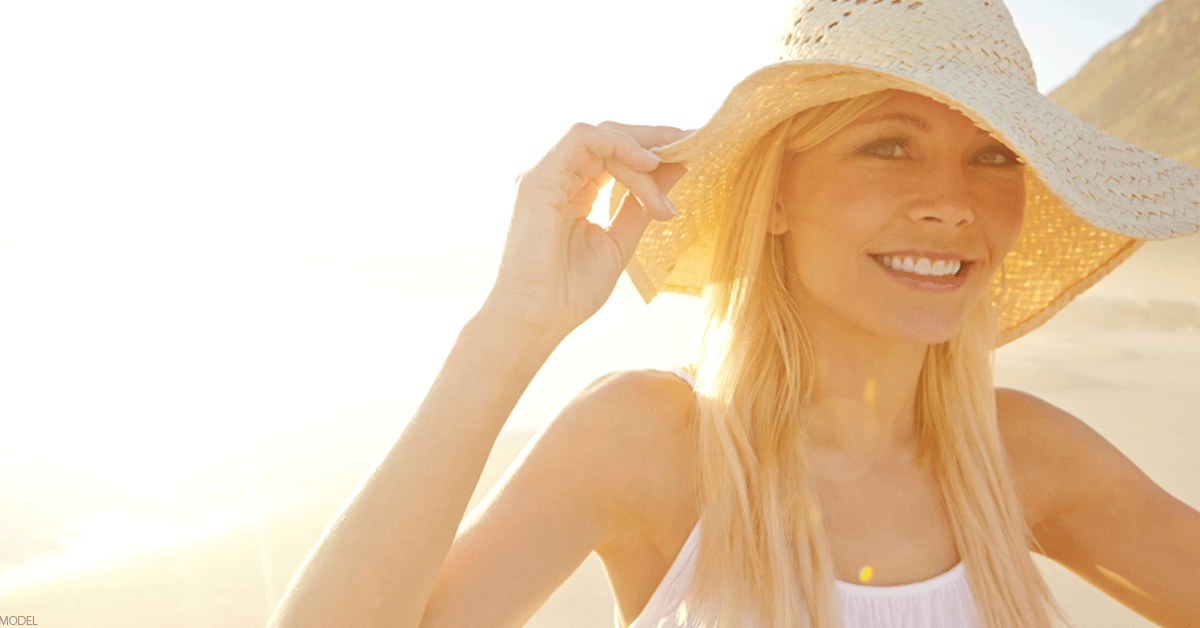 Woman on the beach wearing a sun hat smiling at camera