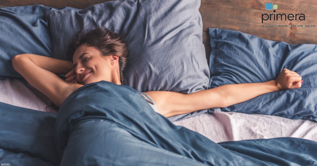 Woman stretches her left arm out while smiling in bed.