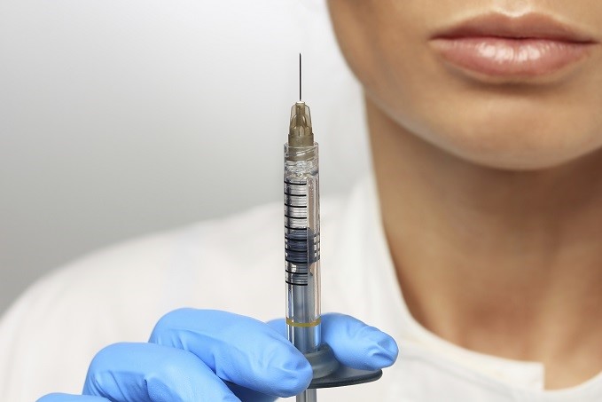 Woman's gloved hand holding needling and syringe