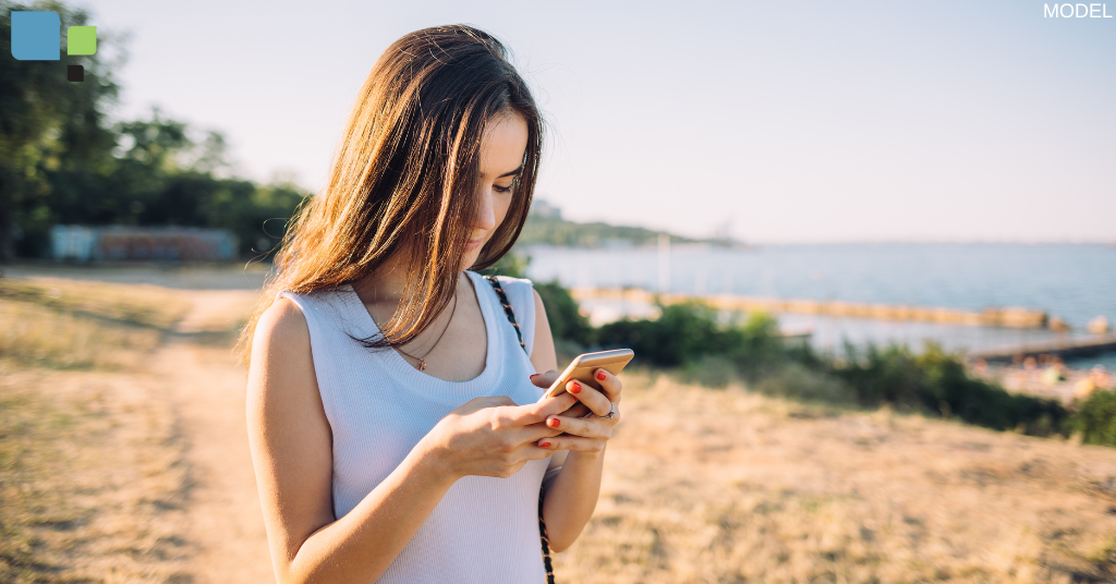 A woman walking outside while looking at her phone (model)