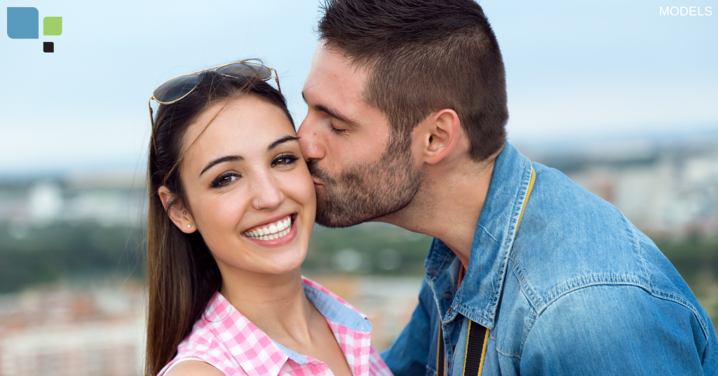 A man kissing a woman on her cheek while she smiles at the camera (models)