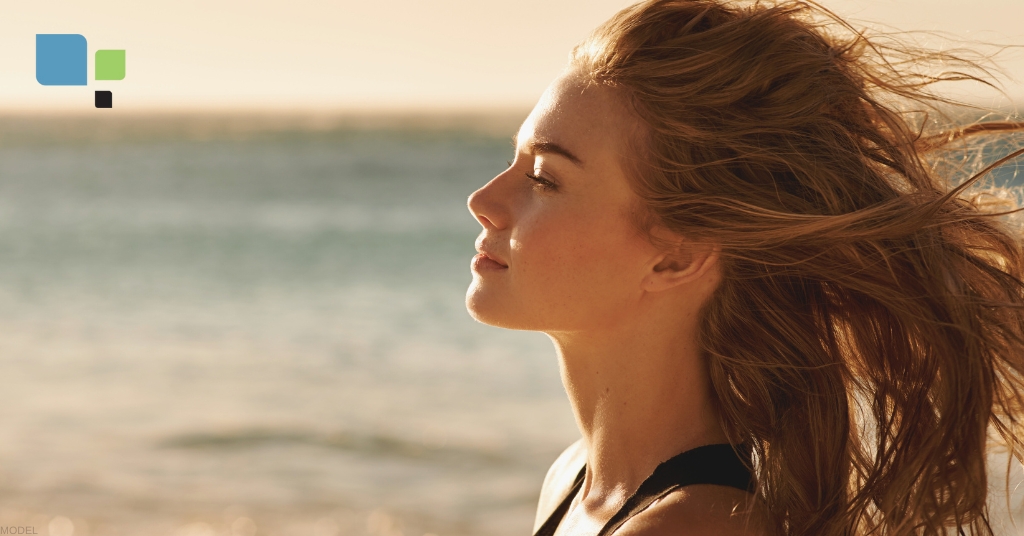 Woman standing on the beach with their hair blowing in the wind (model)