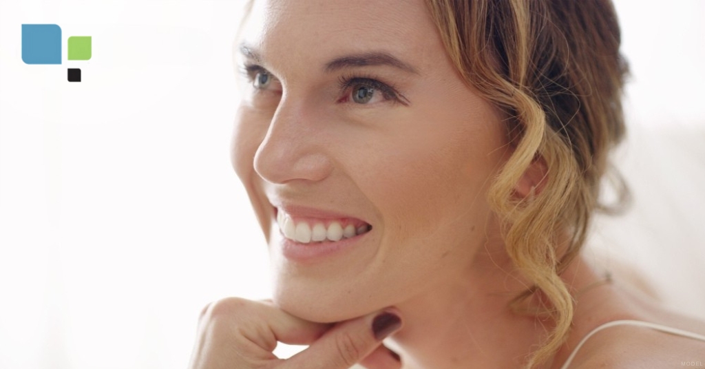 a close up of a woman smiling with their hand on her chin (model) Primera Plastic Surgery Logo